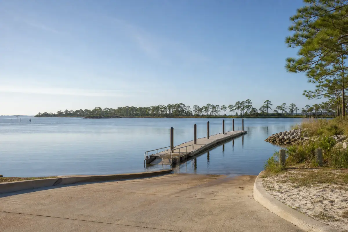 An illustration of a public boat ramp with a concrete slope and a floating dock on a calm bayou, pines on the far shore, for Alaqua Park