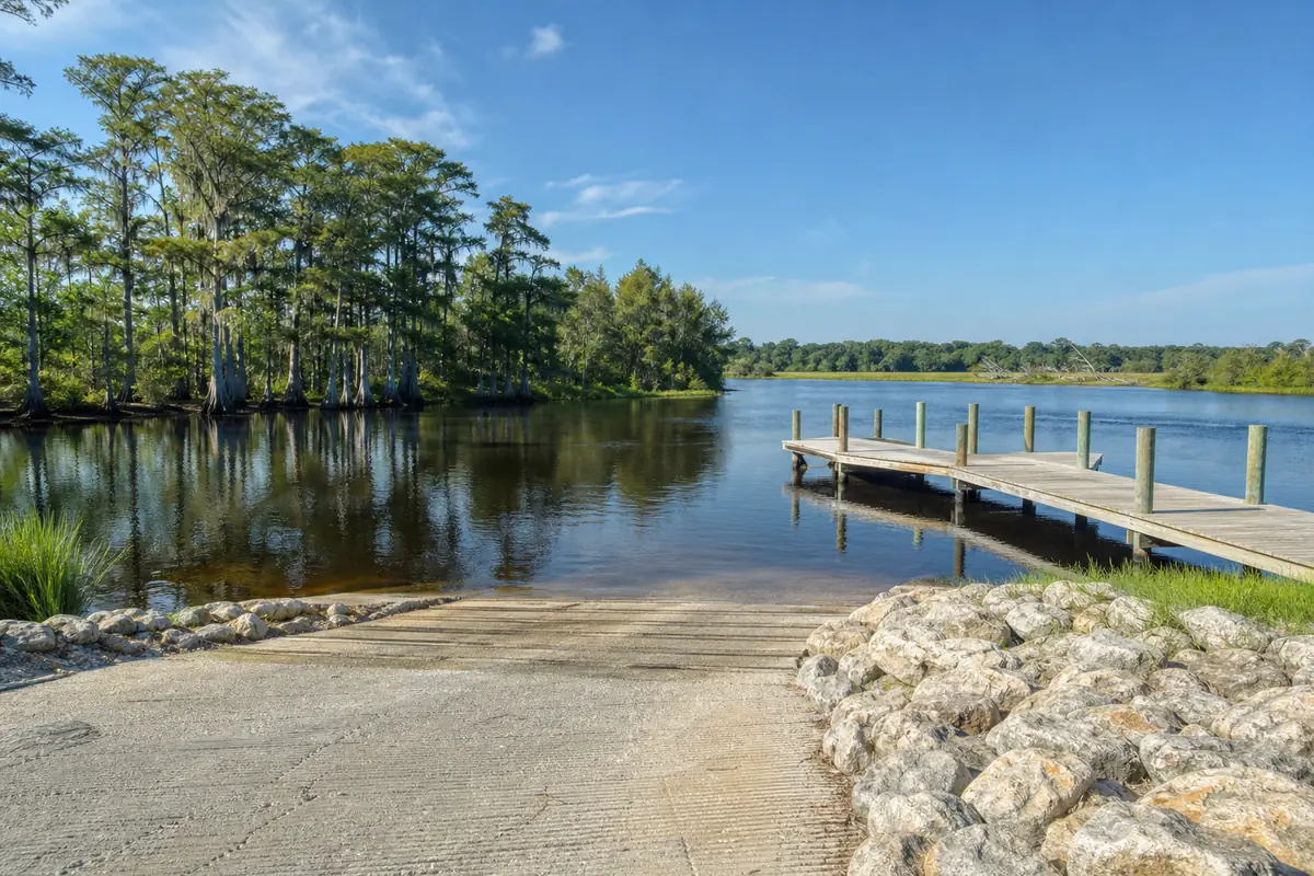 An illustration of a public boat launch on a river bend with a low wooden pier, cypress trees and dark calm water, for Portland Park