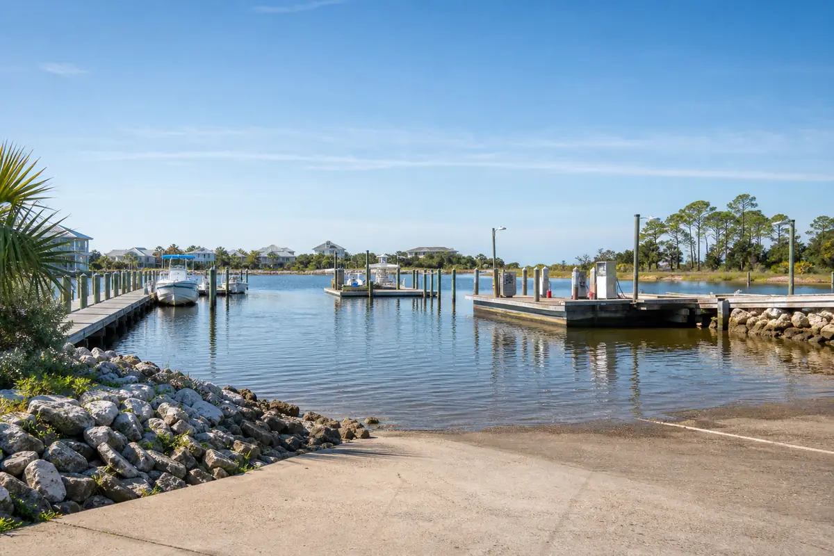 An illustration of a small marina on a calm bayou with a few boat slips, a wooden fuel dock and a launch ramp, for Fishermans Cove Marina