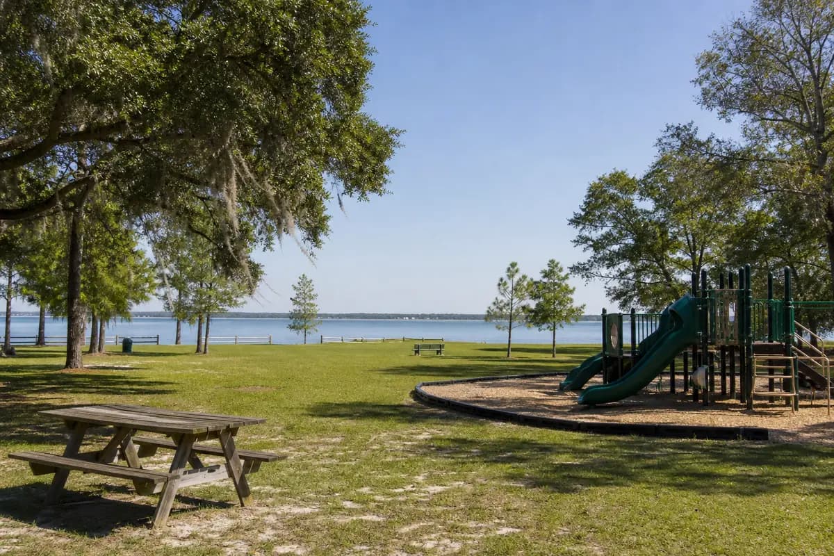 An illustration of a grassy community park with shade trees, a picnic table and a playground at the edge, for Harry A. Laird Park
