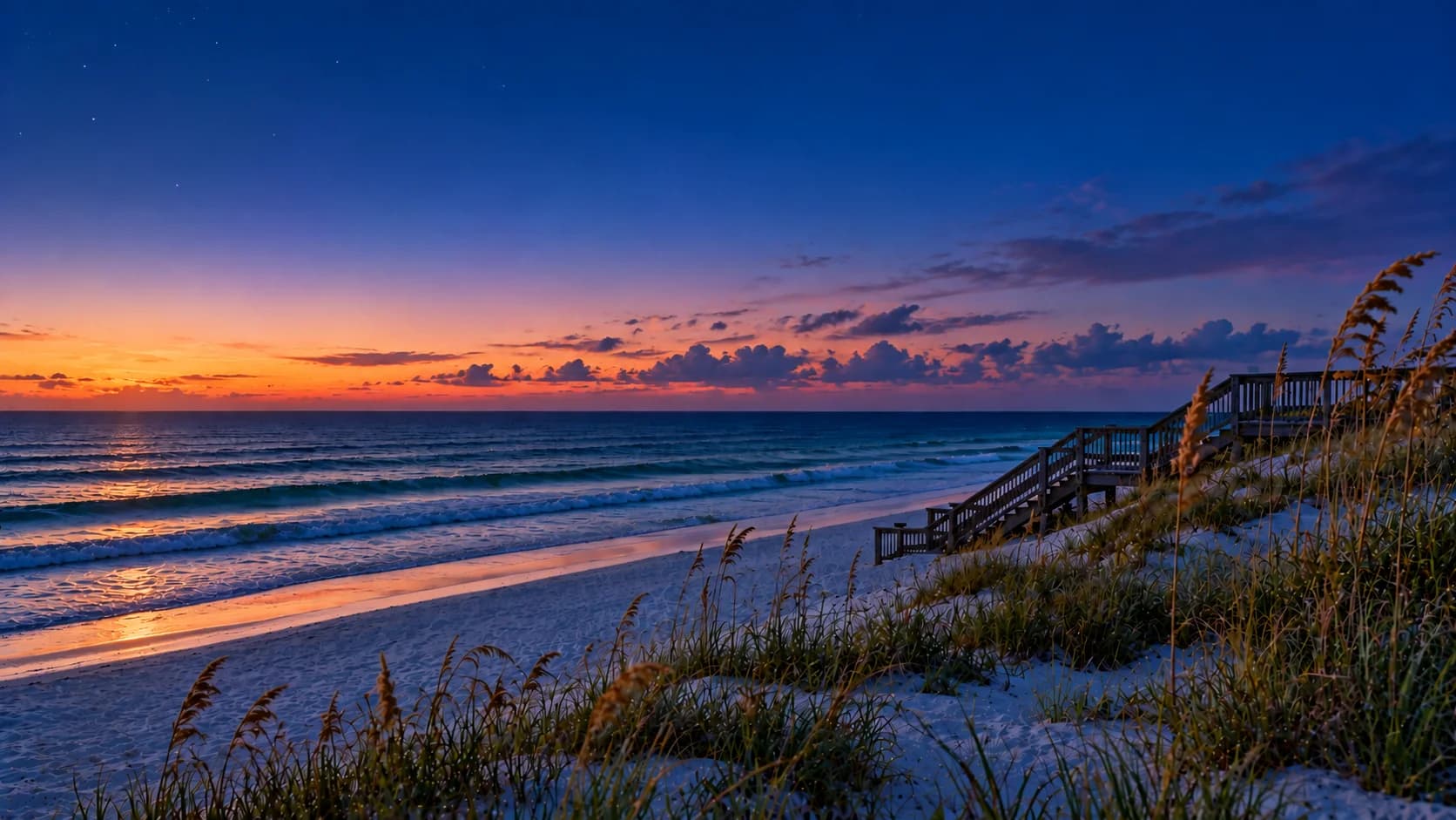 The Gulf at Santa Rosa Beach after sunset: the last orange light along the horizon under a deep blue sky, pale sand and a wooden beach walkover in silhouette.